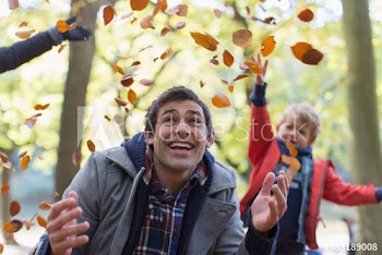 Happy father and son playing and throwing autumn leaves in park