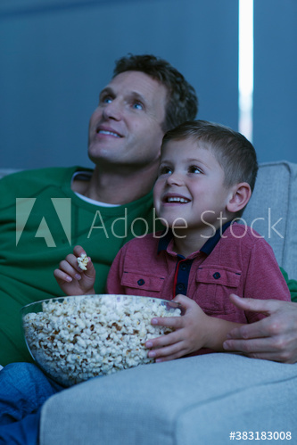 Happy father and son watching movie and eating popcorn on sofa