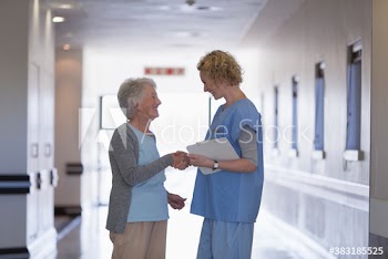 Happy female nurse shaking hands with senior patient in hospital corridor