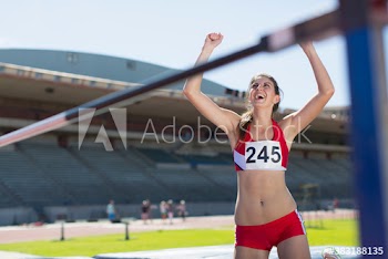 Happy female track and field athlete cheering at high jump