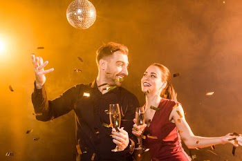 Happy flirting couple with champagne having fun during party under golden light while confetti falling around