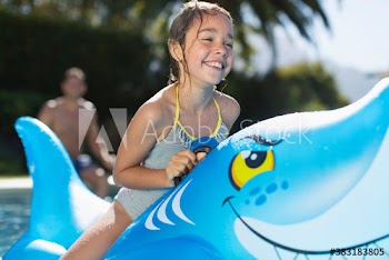 Happy girl on inflatable shark in sunny swimming pool
