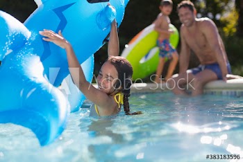 Happy girl playing with inflatable raft in sunny swimming pool