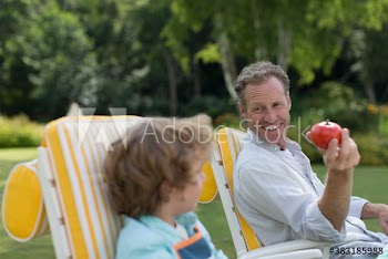 Happy grandfather and grandson with apple in garden