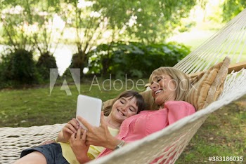 Happy grandmother and granddaughter with digital tablet in hammock