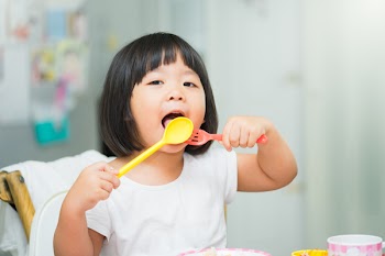 Happy Little asian girl eating fried egg and she have spoon in her mouth.