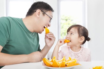 Happy little girl with father eating orange