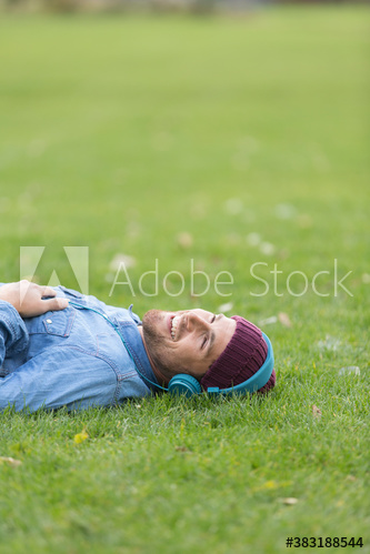 Happy man with headphones listening to music and relaxing in grass