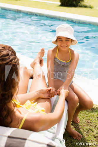Happy mother and daughter holding hands on sunny poolside lounge chair