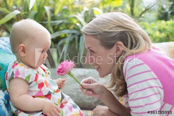 Happy mother showing pink rose to baby daughter