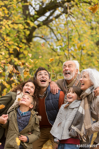Happy multi-generation family watching falling autumn leaves in park