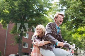 Happy playful young couple riding bicycle in park