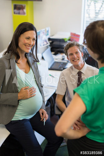 Happy pregnant businesswoman talking with colleagues in office