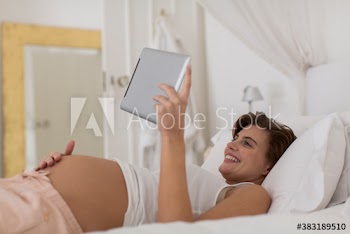 Happy pregnant woman relaxing on bed with digital tablet