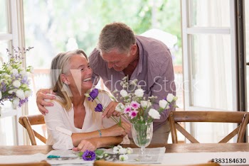 Happy senior couple arranging flowers at table