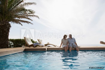 Happy senior couple dipping legs in swimming pool