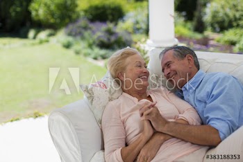 Happy senior couple holding hands and cuddling on patio sofa