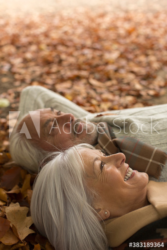 Happy senior couple laying in autumn leaves