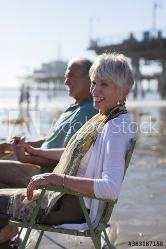 Happy senior couple relaxing in lawn chairs on sunny beach