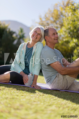 Happy senior couple resting on yoga mat in sunny grass