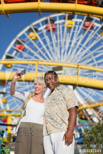 Happy senior couple taking selfie below sunny Ferris Wheel