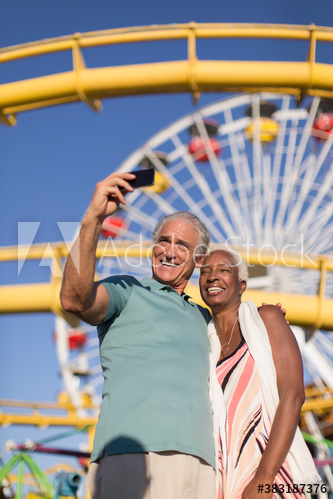 Happy senior couple taking selfie below sunny Ferris Wheel