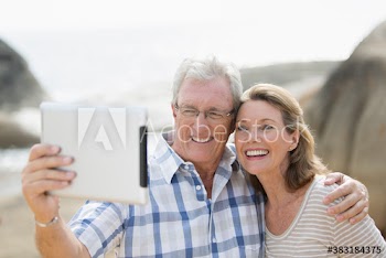 Happy senior couple taking selfie with digital tablet on beach