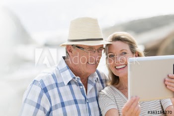 Happy senior couple taking selfie with digital tablet on sunny beach