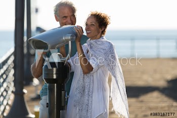 Happy senior couple using coin-operated binoculars on sunny pier