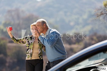 Happy senior couple video chatting outside car at sunny roadside