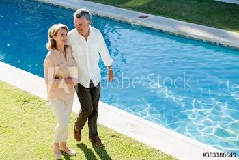 Happy senior couple walking along sunny swimming pool