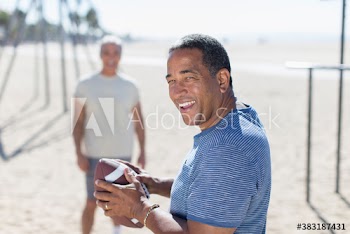 Happy senior man playing football with friend on sunny beach