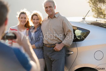 Happy senior parents and daughter posing for photograph at car