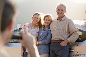 Happy senior parents and daughter posing for photograph at car