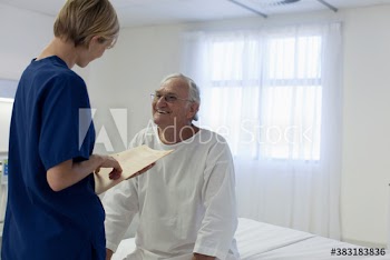 Happy senior patient talking with nurse in hospital room