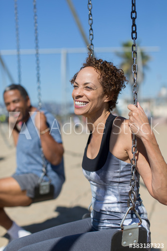Happy senior woman on swing set on sunny beach