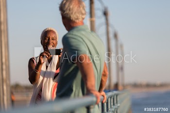 Happy senior woman photographing husband on sunny pier