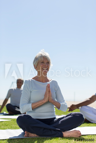 Happy senior woman practicing yoga meditation on sunny lawn