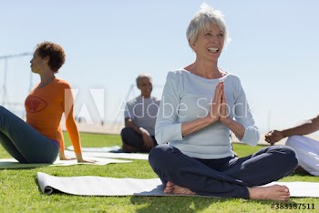 Happy senior woman practicing yoga with friends in sunny grass