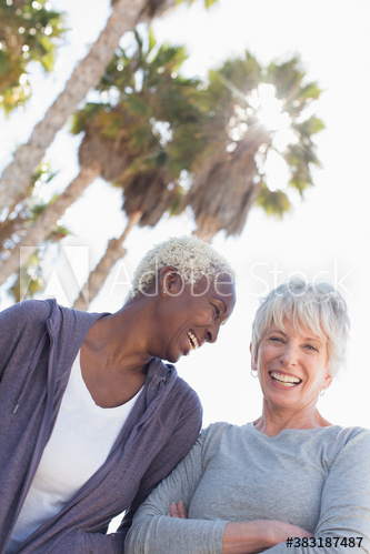 Happy senior women friends below sunny palm trees