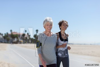 Happy senior women jogging on sunny beach boardwalk