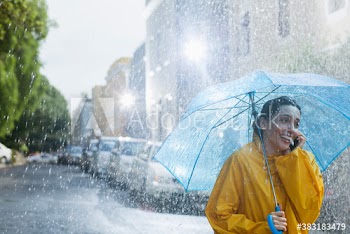 Happy woman with umbrella talking on smart phone on rainy street