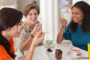 Happy women friends sharing chocolate cake in cafe