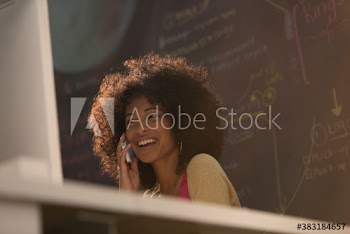 Happy young businesswoman talking on smart phone at computer