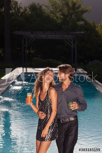 Happy young couple enjoying cocktails at poolside