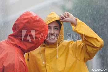 Happy young couple in raincoats standing in rain
