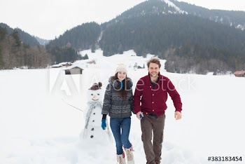 Happy young couple in snowy field with snowman