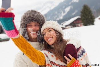 Happy young couple in warm clothing taking selfie in snow