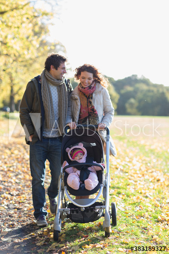 Happy young couple pushing baby daughter in stroller in autumn park
