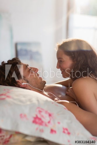 Happy young couple sharing headphones and listening to music on bed